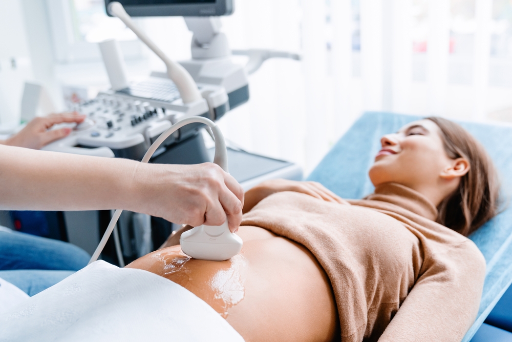 A smiling pregnant woman lies on an examination bed while a healthcare provider conducts an abdominal ultrasound - Ultrasound