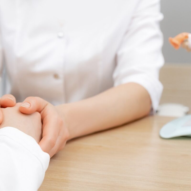 A healthcare professional holds a patient’s hands during a consultation, with a model of the female reproductive system visible on the table - Tubal ligation