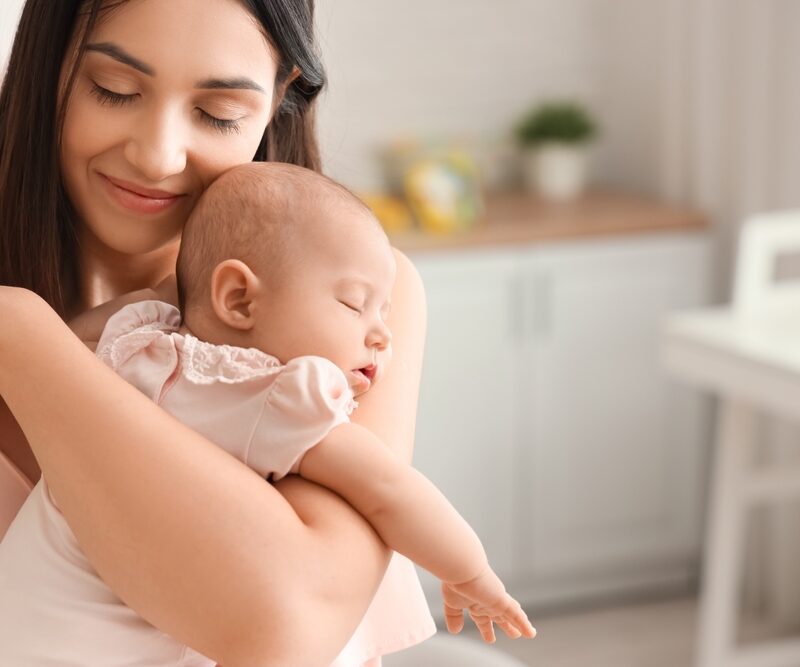 A mother gently holds her sleeping baby in a cozy home setting, radiating love and warmth - Breastfeeding