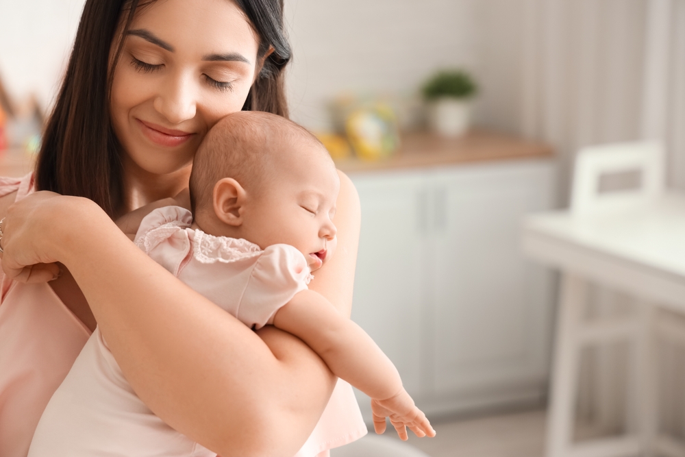 A mother gently holds her sleeping baby in a cozy home setting, radiating love and warmth - Breastfeeding