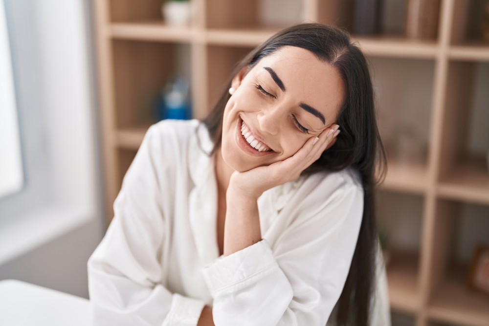 A smiling woman with her eyes closed, resting her head on her hand in a relaxed and content pose - Physicians for Women - Melius Schurr A smiling woman with her eyes closed, resting her head on her hand in a relaxed and content pose - Physicians for Women - Melius Schurr