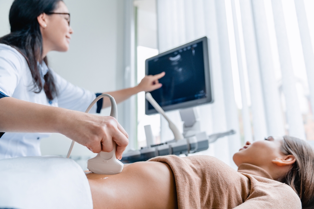 A doctor performing an ultrasound scan on a patient's abdomen, with the screen showing the scan results - Physicians for Women - Melius Schurr A doctor performing an ultrasound scan on a patient's abdomen, with the screen showing the scan results - Physicians for Women - Melius Schurr