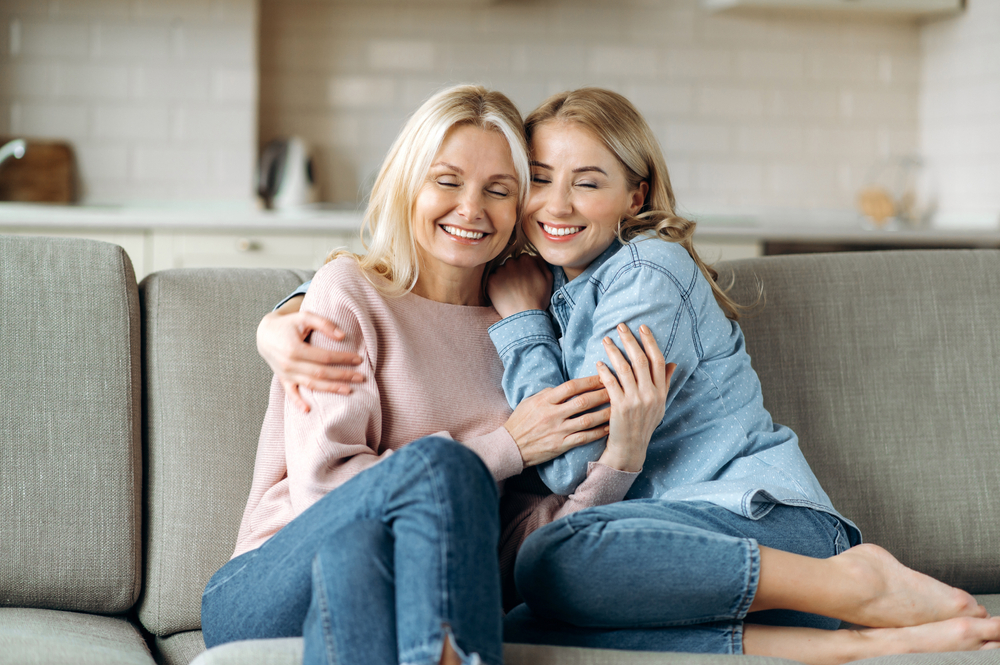 A mother and daughter sit on a couch, embracing each other with warm smiles - Physicians for Women - Melius Schurr A mother and daughter sit on a couch, embracing each other with warm smiles - Physicians for Women - Melius Schurr
