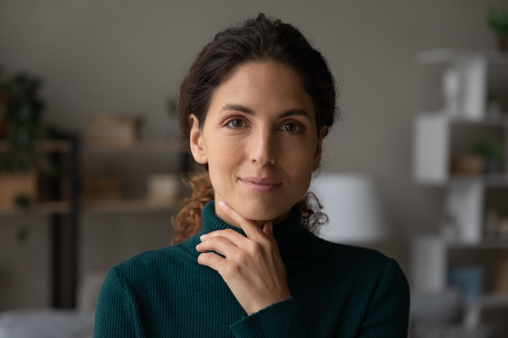 A thoughtful woman in a green sweater looking directly at the camera, resting her hand under her chin - Physicians for Women - Melius Schurr A thoughtful woman in a green sweater looking directly at the camera, resting her hand under her chin - Physicians for Women - Melius Schurr